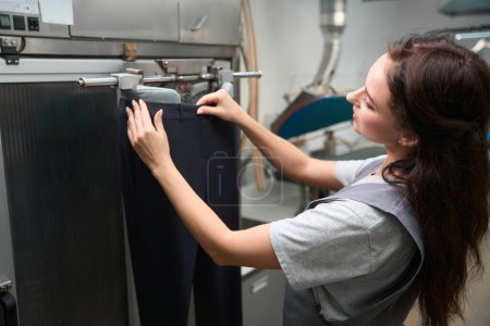 Photo for Dry-cleaning service operator wearing pants on automatic ironing mannequin, processing clothes after washing - Royalty Free Image