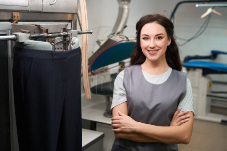 Photo for Attractive woman laundry office worker smiling standing near automatic ironing mannequin, professional pants ironing - Royalty Free Image