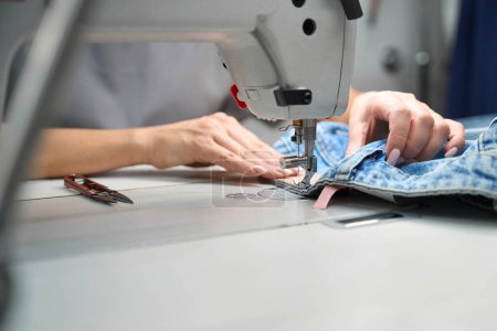 Photo for Professional seamstress sewing tags to clothes on sewing machine, post-treatment after dry-cleaning, alteration service - Royalty Free Image