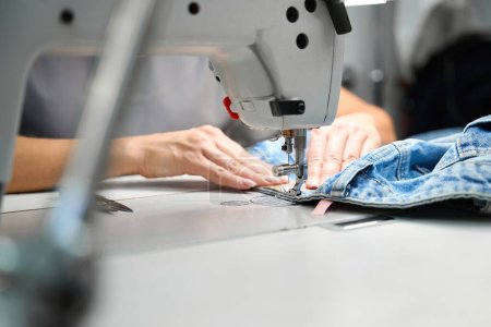 Foto de Sastre femenino trabajando en la máquina de coser, agregando etiquetas a la ropa después de la limpieza en seco, remendar agujeros, servicio de alta calidad - Imagen libre de derechos