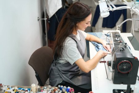 Foto de Mujer sonriente que adapta y altera la ropa en la máquina de coser industrial, servicio de limpieza en seco - Imagen libre de derechos