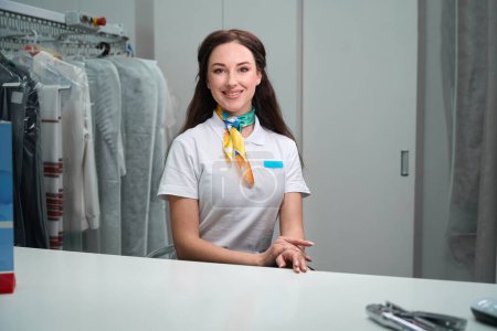Photo for Cheerful woman dry-cleaning office administrator waiting for clients to take garments for cleaning, - Royalty Free Image