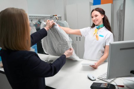 Téléchargez les photos : Femme cliente recevant son vêtement propre à la réception du bureau de nettoyage à sec, qualité et service rapide - en image libre de droit