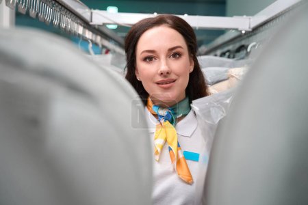 Photo for Beautiful woman administrator of dry-cleaning office standing between racks with clean and fresh garment on hangers, quality service - Royalty Free Image