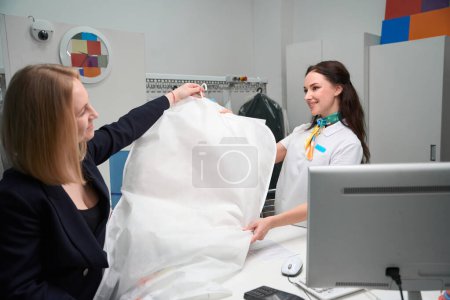 Foto de Cliente femenino de limpieza en seco que recupera la prenda limpia en una cubierta especial del administrador en recepción - Imagen libre de derechos