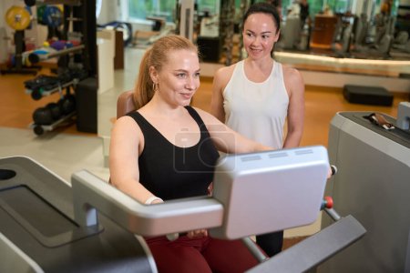 Photo for Two joyful female are in the gym of the fitness clinic, the blonde is engaged in the simulator - Royalty Free Image