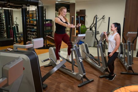 Foto de Dos mujeres están en el gimnasio de una clínica de fitness, moderno equipo de fitness está alrededor - Imagen libre de derechos