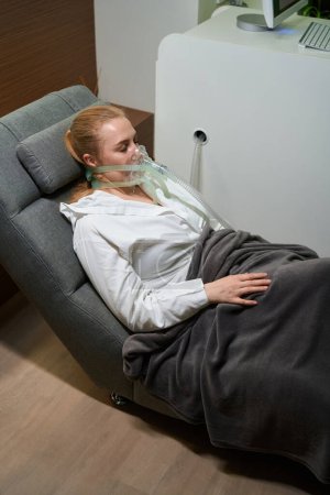 Photo for Woman in a special mask sits in a comfortable chair, she enjoys the hypoxic therapy procedure - Royalty Free Image
