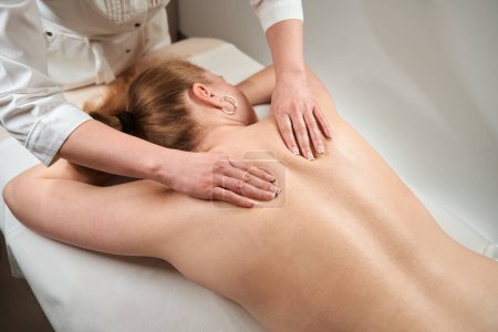 Foto de Masajista en la clínica hace un masaje manual a un cliente, una mujer con una espalda desnuda se encuentra en la mesa de masaje - Imagen libre de derechos