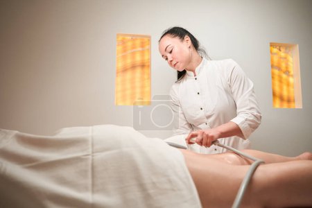 Téléchargez les photos : Masseur femelle fait un massage des pieds matériel au client, le spécialiste utilise un équipement moderne - en image libre de droit