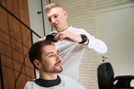 Foto de Cliente en una silla de peluquería en el peinado, el maestro tiene un reloj inteligente - Imagen libre de derechos