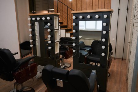 Téléchargez les photos : Salon de coiffure respectueux de l'environnement dans un salon de coiffure avec un design minimaliste moderne, miroirs, chaises en cuir, excellent éclairage - en image libre de droit