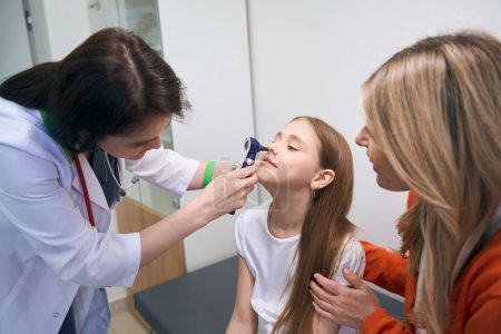 Photo for Woman ear, nose and throat specialist using otoscope with light to check condition of little girl nose, medical exam in private clinic - Royalty Free Image