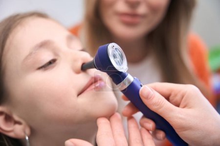 Photo for Close-up professional laryngologist checking girl patient health, examining nose with specialized tool, regular pupils health check-up - Royalty Free Image