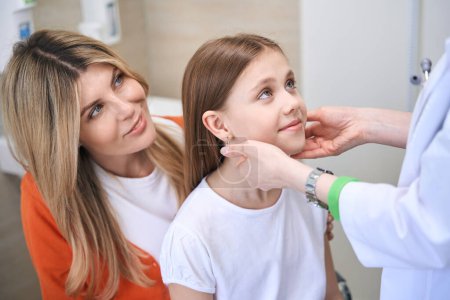 Photo for Caring laryngologist examining llittle girl lymph nodes during health check-up, satisfied with girl health - Royalty Free Image