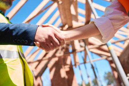 Photo for Contractor and building engineer shaking hands on background of roof beams, making deal for building construction, close-up - Royalty Free Image