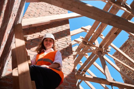 Téléchargez les photos : Femme souriante chef de projet debout sur l'échelle et regardant le chantier de construction, inspecteur en casque de sécurité vérifiant la qualité du bâtiment, développement de logements - en image libre de droit