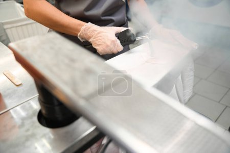 Foto de Trabajador de limpieza en seco tratando la ropa con vapor, quitando manchas y cuidadosamente planchando pliegues, primer plano - Imagen libre de derechos