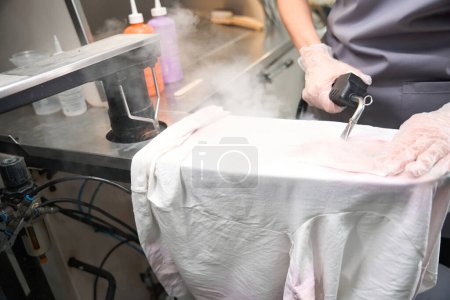 Foto de Limpieza en seco calificada eliminación de manchas de prendas blancas con pistola de vapor, tratamiento previo, lavandería profesional - Imagen libre de derechos