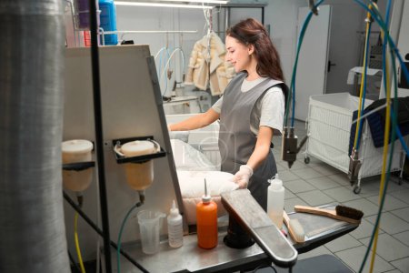 Photo for Happy smiling woman dry-cleaning worker carefully examining item after cleaning, satisfied with her job, professional laundry service - Royalty Free Image