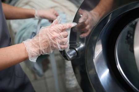 Foto de Close-up mujer servicio de limpieza en seco operador de cierre de la máquina de tambor después de cargar la ropa en el interior, lavandería sin agua - Imagen libre de derechos