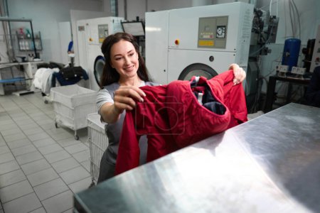 Téléchargez les photos : Femme blanchisseuse de bureau souriant, regardant veste propre, satisfaite des taches enlevées, nettoyage sans eau - en image libre de droit