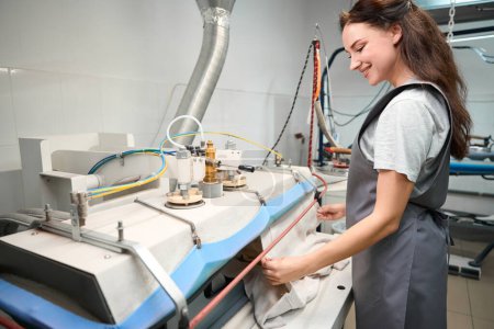 Photo for Smiling woman laundry service worker using steam press for shaped-fixing and ironing process, professional ironing - Royalty Free Image