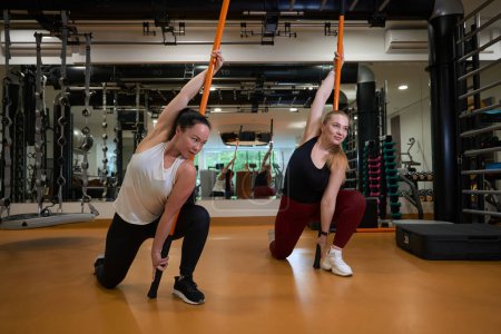 Foto de Rubia y una morena en ropa deportiva realizan ejercicios con palos gimnásticos, utilizan cómodos karimats - Imagen libre de derechos