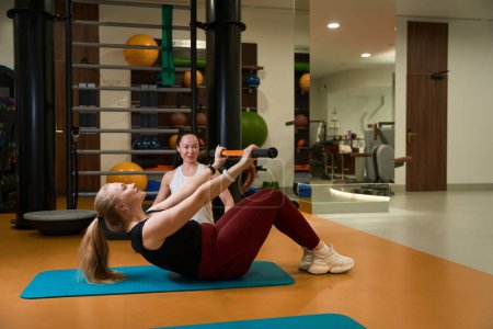 Foto de Mujer realiza ejercicios eficaces con un palo de gimnasia, junto a un entrenador de fitness - Imagen libre de derechos