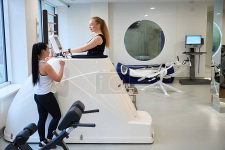 Photo for Woman trainer of clinic helps a client in the fitness room, women in sportswear - Royalty Free Image