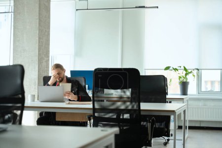Foto de El hombre barbudo trabaja en un ordenador portátil en una habitación luminosa, la habitación tiene un interior minimalista - Imagen libre de derechos