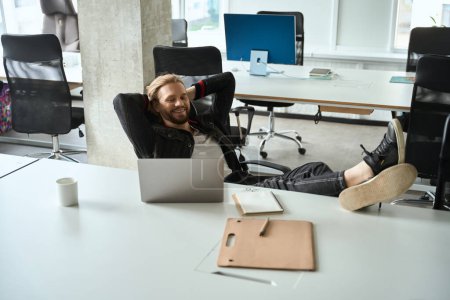 Photo for Satisfied guy comfortably settled down in a coworking space with a laptop, he put his feet on the table - Royalty Free Image