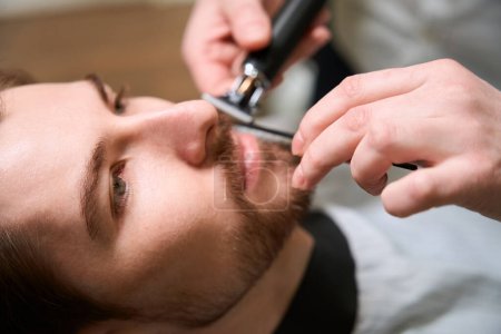 Téléchargez les photos : Barbier expérimenté au travail s'occupant d'un client barbe et moustache, un professionnel utilise un outil spécial - en image libre de droit