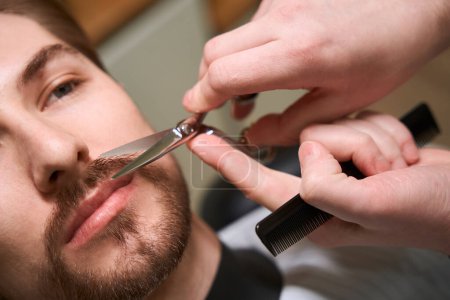 Foto de Peluquero corta clientes bigote con tijeras especiales, el hombre prefiere el cuidado profesional del cabello facial - Imagen libre de derechos