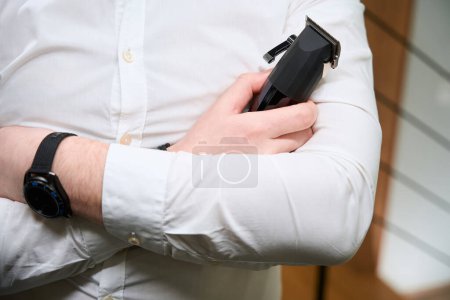 Foto de El hombre con una camisa ligera sostiene un clipper en sus manos, el maestro utiliza aparatos modernos - Imagen libre de derechos