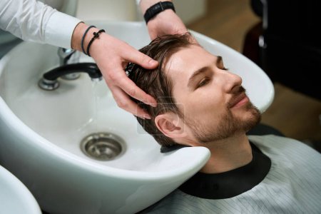 Foto de Peluquería cliente disfruta del proceso de lavado del cabello, peluquería trabaja en un lugar de trabajo bien equipado - Imagen libre de derechos