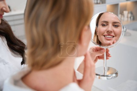 Photo for Happy female blonde looks in the mirror at a consultation with an esthetician, she is pleased with the reflection in the mirror - Royalty Free Image