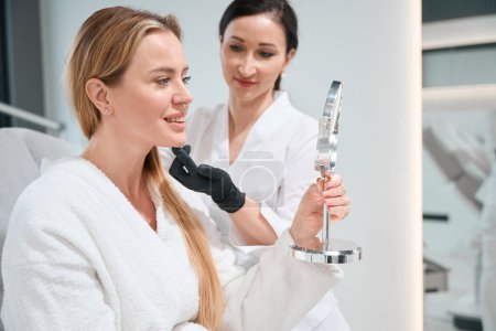 Patientin einer kosmetologischen Klinik untersucht ihr Gesicht nach Anti-Aging-Verfahren im Spiegel