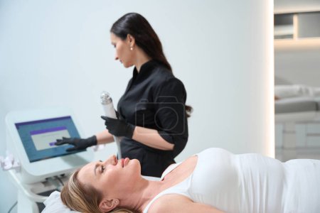 Photo for Cosmetologist sets up the device for the RF lifting procedure, the specialist uses modern equipment - Royalty Free Image