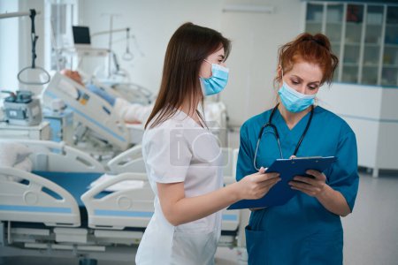 Foto de Médico profesional y enfermera en máscara médica revisando nuevo análisis del paciente en la sala de hospitalización - Imagen libre de derechos