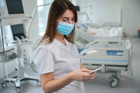 Photo for Portrait of the beautiful female doctor using her mobile phone while standing in intensive care unit - Royalty Free Image