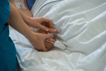 Foto de Foto recortada del trabajador médico utilizando oxímetro de pulso con el paciente hospitalizado para comprobar el nivel de oxígeno en la sangre en reanimación - Imagen libre de derechos