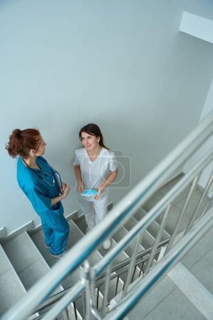 Téléchargez les photos : Deux ambulanciers communiquent entre eux pendant la pause déjeuner sur l'escalier de la clinique - en image libre de droit