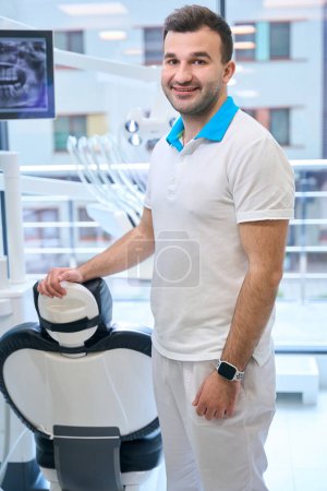 Photo for Cute male at the workplace in a modern dental office, the doctor has a smart watch - Royalty Free Image