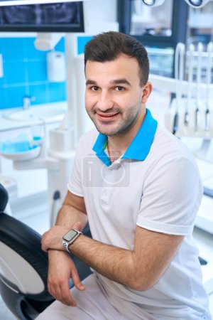 Téléchargez les photos : Brunette homme sur le lieu de travail dans un cabinet dentaire moderne, équipement moderne autour - en image libre de droit