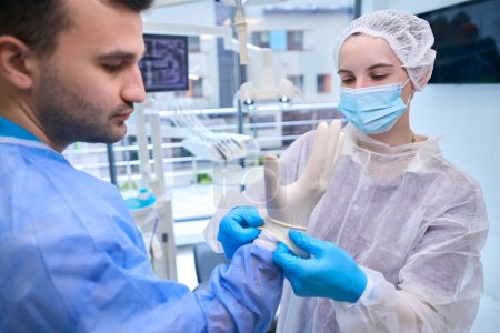 Photo for Woman assistant puts on the doctor disposable sterile gloves, the team is preparing for the operation - Royalty Free Image