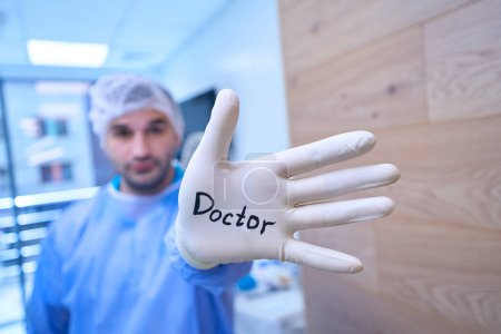 Foto de Cirujano masculino en un guante desechable con la inscripción Doctor, junto a una asistente femenina - Imagen libre de derechos