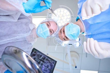 Foto de Cirujano y asistente en uniforme médico están en el quirófano, la sala es ligera y estéril - Imagen libre de derechos