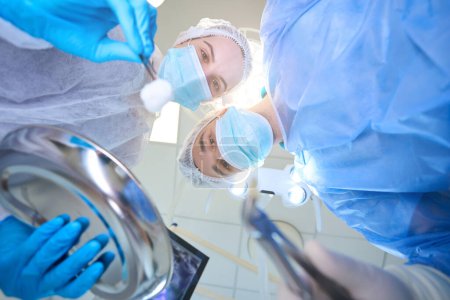 Téléchargez les photos : Jeune chirurgien tient des pinces avec une dent enlevée, une assistante a une pince à épiler avec un écouvillon dans les mains - en image libre de droit