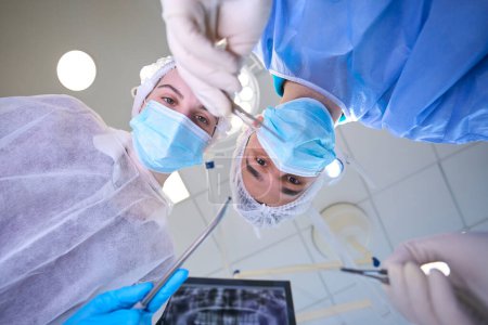Foto de El cirujano masculino sostiene una aguja quirúrgica especial en sus manos, una asistente femenina está cerca - Imagen libre de derechos